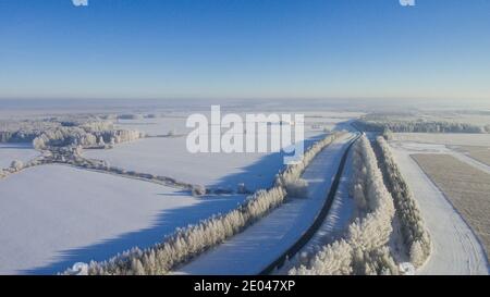 Strada invernale lungo i campi tra le città vista aerea da un drone. Paesaggio invernale da un drone. Vista invernale sulla strada da un drone Foto Stock