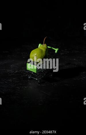 pera nel minuscolo carrello supermercato su nero. Il concetto di alimentazione sana Foto Stock