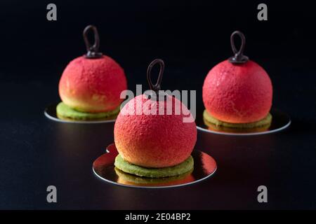 Tre dolci mousse sotto forma di palle di Natale su sfondo scuro. Foto Stock