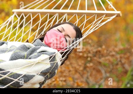 Donna con maschera due covid 19 dormendo sdraiato su amaca in autunno Foto Stock