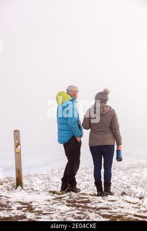 Uomo e donna che camminano lungo il sentiero della pietra arenaria su Bosley Cloud Vicino a Congleton a Cheshire nella neve e nebbia d'inverno Foto Stock