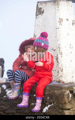 Due ragazze sedettero a parlare seduto sul punto di trig O punto di triangolazione sulla cima di Bosley Cloud vicino Congleton Cheshire nella neve d'inverno Foto Stock