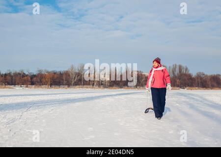 Donna anziana che trasporta la slitta dopo che slitta giù. Donna che si diverte sul fiume ghiacciato invernale. Foto Stock