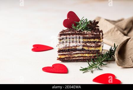 Il pezzo di torta stratificata di cioccolato e cuori rossi su fondo di cemento chiaro. Decorazioni festive per il giorno di San Valentino. Torta di miele russa, Medovik. Selettivo Foto Stock