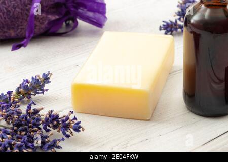 Aromaterapia spa e prodotti per l'igiene naturale concetto con sapone fatto in casa circondato da sacchetto viola di lavanda secca, fiori viola e una bott marrone Foto Stock