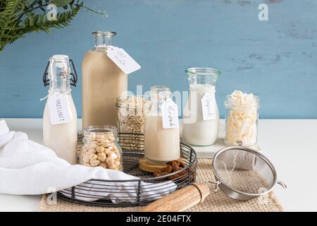 Bottiglie di latte alternativo etichettato in su un tovaglia rustico. Vasi di cristallo pieni di semi, cereali e noci sono accanto a loro. Foto Stock