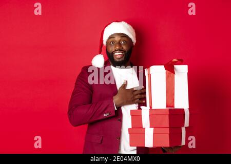 Natale, Capodanno e concetto di shopping. Felice uomo nero ricevere regali di Natale, dicendo grazie e sorridendo grato, in piedi in cappello di santa contro Foto Stock