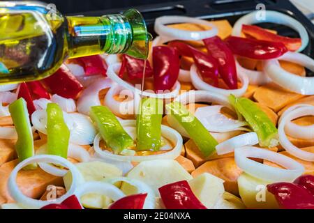 Bottiglia di olio d'oliva versato su verdure crude tritate un vassoio da forno Foto Stock