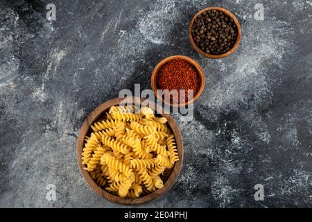 Pasta di fusilli grezza in ciotola di legno con spezie al pepe Foto Stock