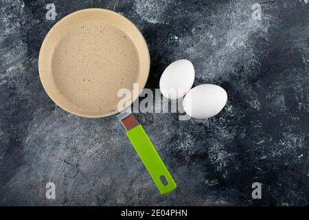 Uova bianche grezze accanto alla padella vuota Foto Stock
