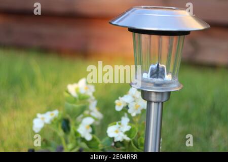 Vista in primo piano su una lampada solare in un giardino accanto a fiori bianchi Foto Stock