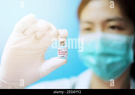 Una donna asiatica medico con maschera chirurgica e guanti di gomma bianca in una clinica, tenendo un flacone di vetro di 1 dose vaccino ROTA con fondo bianco A. Foto Stock