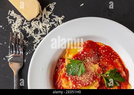 Immagine piatta di piatto di porcellana bianca di Ravioli italiani in salsa di pomodoro finito con parmigiano grattugiato e foglie di prezzemolo verde fresco. Un chee Foto Stock