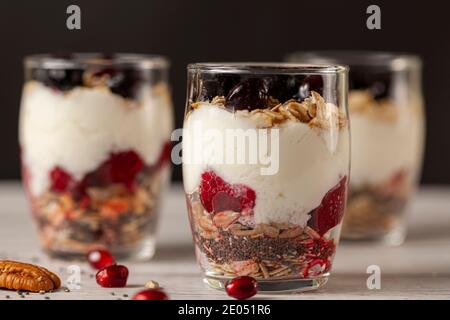 Vista laterale di deliziosi bicchieri di parfait di frutta e yogurt ripieni di strati di muesli, semi di chia, frutti di bosco freschi, avena arrotolata e yogurt fatto in casa serviti Foto Stock