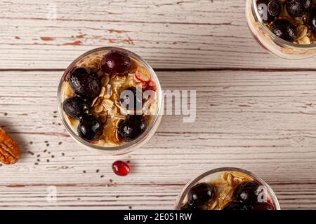 Immagine piatta di deliziosi bicchieri da parfait di yogurt alla frutta ripieni di muesli, semi di chia, frutti di bosco freschi, avena arrotolata e yogurt fatto in casa serviti Foto Stock