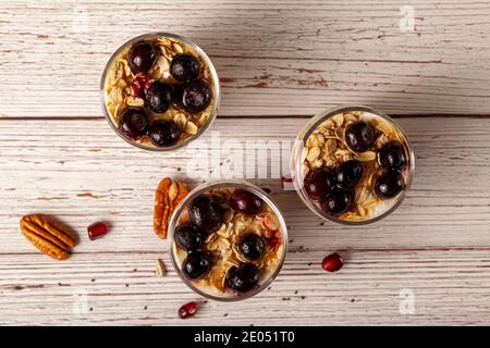 Immagine piatta di deliziosi bicchieri da parfait di yogurt alla frutta ripieni di muesli, semi di chia, frutti di bosco freschi, avena arrotolata e yogurt fatto in casa serviti Foto Stock