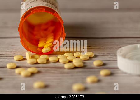 Una bottiglia di farmaco di prescrizione arancione capovolta sopra sul tavolo di legno con le pillole rotonde gialle sparse sulla superficie. Un'immagine versatile per la salute, Foto Stock