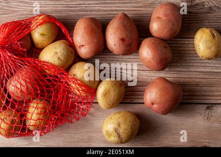 Immagine ravvicinata piatta con un sacco di patate in mesh rossa con patate biologiche crude rosa e gialle su sfondo di legno. Un alimento versatile per la natura morta Foto Stock