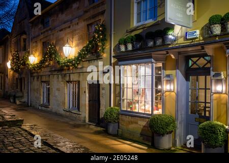 La Covent Garden Academy of Flowers lungo la strada principale con le luci di natale all'alba. Chipping Campden, Cotswolds, Gloucestershire, Inghilterra Foto Stock