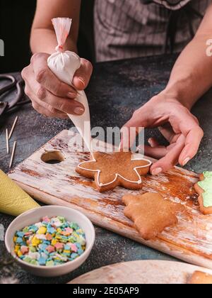 Donna decorare i biscotti di pan di zenzero. Dolci di Natale tradizionali fatti in casa. Delizioso dessert. Le mani delle persone si avvicinano. Shot verticale Foto Stock