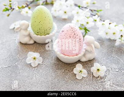 Uova di Pasqua colorate in piedi con figurine coniglietto di pasqua in ceramica e fioritura primaverile su fondo grigio in cemento Foto Stock