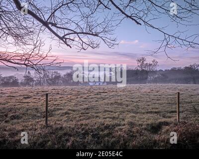 Un campo ghiacciato all'alba. Gli strati di nebbia si depositano sopra il terreno più basso attraverso una vista classica della campagna britannica all'alba in inverno. Foto Stock