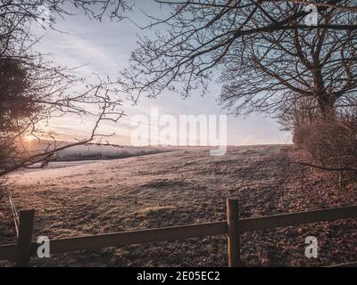 Un campo ghiacciato all'alba. Gli strati di nebbia si depositano sopra il terreno più basso attraverso una vista classica della campagna britannica all'alba in inverno. Foto Stock