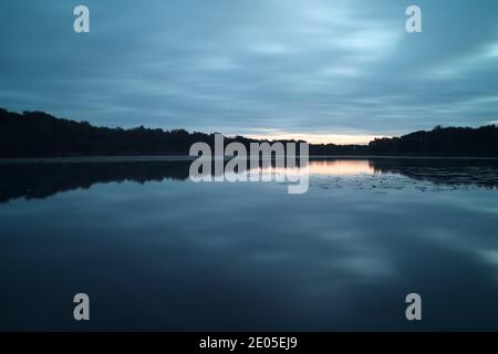 Una lunga esposizione scattata nel tempo prima dell'alba cattura una scena di suoni blu e grigi sommersi che si riflettono nell'acqua still di Hatch Pond Foto Stock