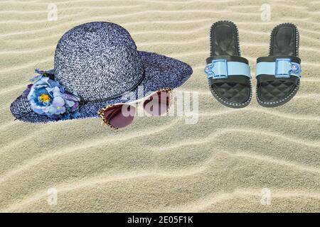 Cappello di paglia, occhiali da sole e infradito sulla spiaggia di sabbia. Sfondo per vacanze estive e viaggi pubblicitari con spazio. Concetto di vacanza in spiaggia. Foto Stock