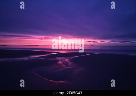 Il sole che sorge riempie un cielo invernale di colore sulle piscine maree incise sulla sabbia bagnata della spiaggia di Bournemouth. Foto Stock