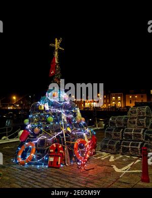 L'albero di Natale dei pescatori tradizionali si è illuminato al porto di Arbroath con le barche e le case sullo sfondo. Foto Stock