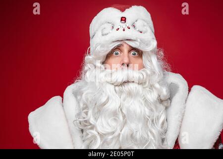Sorpresa scioccato Babbo Natale, chiedendosi uomo anziano con barba grigia, primo piano studio ritratto su sfondo rosso Foto Stock