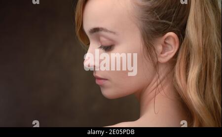 Un ritratto di bellezza paesaggistica primo piano di una giovane donna naturalmente bella (20) guardando a lato e verso il basso con spazio di copia. Foto Stock
