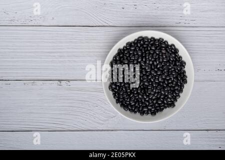 Fagioli neri in ciotola bianca su sfondo di legno bianco. Vista dall'alto. Concetto di cibo vegano Foto Stock