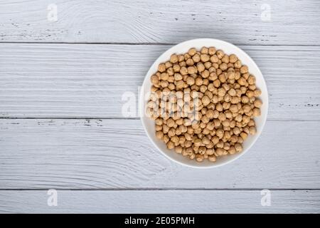 Ceci secchi non cotti in ciotola su tavolo di legno bianco. Mucchio di legume chickpea sfondo. Vista dall'alto. Concetto di cibo vegano Foto Stock