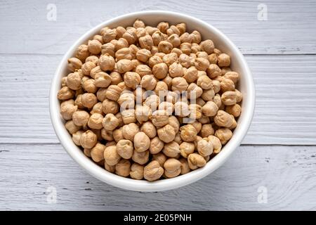 Ceci secchi non cotti in ciotola su tavolo di legno bianco. Mucchio di legume chickpea sfondo. Vista dall'alto. Concetto di cibo vegano Foto Stock