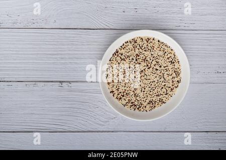 Quinoa crude mista in ciotola su tavolo da cucina in legno bianco. Vista dall'alto. Prodotto alimentare sano e dietetico super. Cibo vegano Foto Stock
