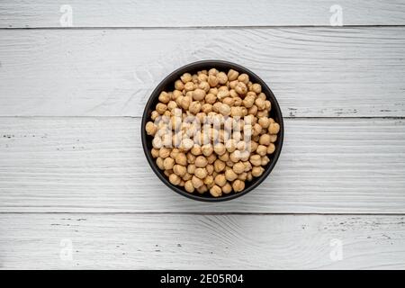 Ceci secchi non cotti in ciotola su tavolo di legno bianco. Mucchio di legume chickpea sfondo. Vista dall'alto. Concetto di cibo vegano Foto Stock