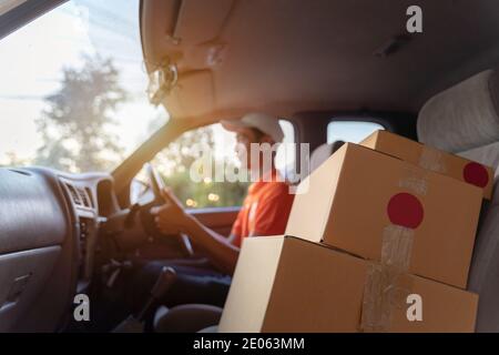 Autista di consegna asiatico, furgone di guida con pacchi sul sedile fuori magazzino. Concetto di trasporto terrestre. Foto Stock