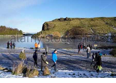 Edimburgo, Scozia, Regno Unito. 30 dicembre 2020. Le persone che si godono la neve all'aperto nel parco Holyrood, visto qui in un Dunsapie Loch ghiacciato e Dunsapie Hill. Credit: Craig Brown/Alamy Live News Foto Stock