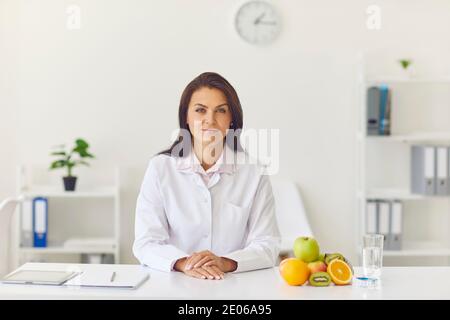 Donna dietista seduto alla scrivania d'ufficio con frutta e misurazione nastro che guarda la fotocamera Foto Stock