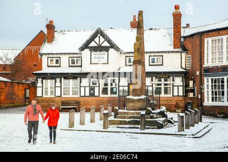 Coppia che cammina mano nella mano accanto alle antiche croci di pietra sassone nella piazza del mercato acciottolata e innevata in inverno a Sandbach, Cheshire, Inghilterra Foto Stock