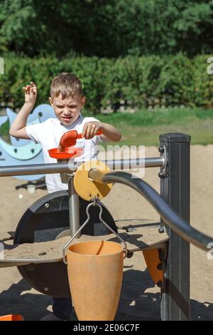 piccolo ragazzo che gioca su un parco giochi con sabbia su un giorno estivo soleggiato Foto Stock