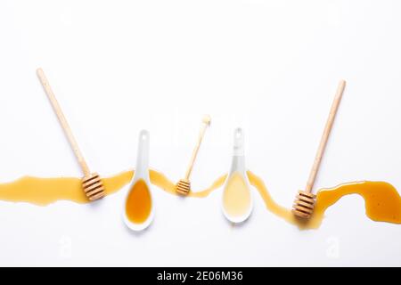 cucchiai bianchi e bastoncini di miele, con miele versato, isolati su fondo bianco Foto Stock