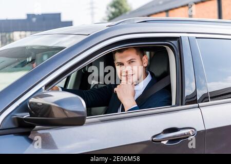 Giovane uomo d'affari sorridente alla macchina fotografica in auto su primo piano sfocato Foto Stock