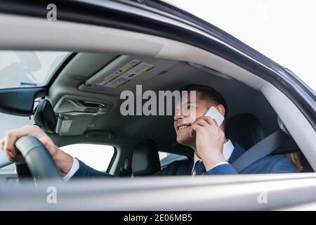 Uomo d'affari allegro che parla con lo smartphone mentre si guida l'auto su offuscato primo piano Foto Stock