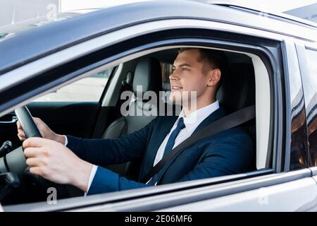 Uomo d'affari sorridente che guida l'auto in primo piano sfocato Foto Stock