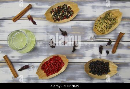 Vista dall'alto su tavola in legno bianco con vetro tonico gin, pepe rosso, fiori di ibisco secchi, bastoncini di cannella, bacche di ginepro, cardamomo natura Foto Stock