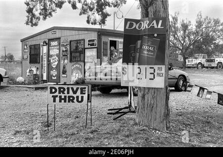 Drive Thru Drive nel fast food 1990s USA. Donna che si piega e serve un cliente nella sua auto. Sweetwater, Texas 1999 US. Il viaggio attraverso l'edificio del fast food coperto da cartelloni pubblicitari per la vendita di sigarette HOMER SYKES Foto Stock