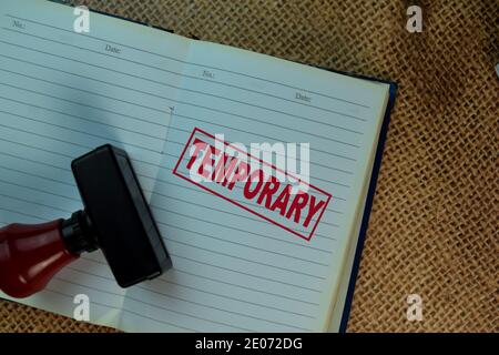 Maniglia rossa stampatore in gomma e testo temporaneo isolato su marrone posa della tela sul tavolo Foto Stock